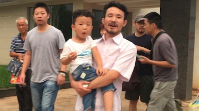 In this June 28, 2017 file image taken from video, Chinese labor activists Hua Haifeng, center, carries his son Bo Bo, and Li Zhao, second left, leave a police station after being released in Ganzhou in southern China's Jiangxi Province. China Labor Watch says three activists who were arrested while investigating abuses at Ivanka Trump's Chinese suppliers last year were released from bail on Tuesday June 26, 2018, but questions remain about their ability to live and work freely.