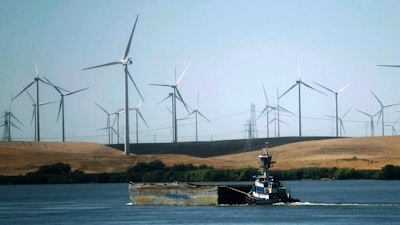 In this Sept. 23, 2013, file photo, a tugboat pushes a barge down the Sacramento River past wind turbines near Rio Vista, Calif. A contentious proposal to link oversight of California's electric grid with other western states faces a crucial test Tuesday, June 19, 2018, in a state Senate committee.