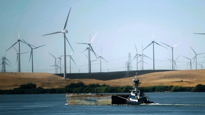 In this Sept. 23, 2013, file photo, a tugboat pushes a barge down the Sacramento River past wind turbines near Rio Vista, Calif. A contentious proposal to link oversight of California's electric grid with other western states faces a crucial test Tuesday, June 19, 2018, in a state Senate committee.