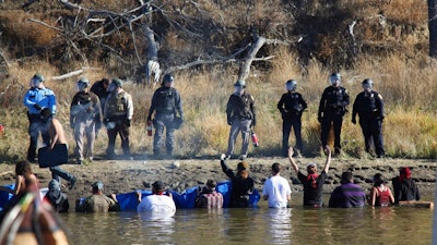 In this Nov. 2, 2016 file photo, protesters demonstrating against the expansion of the Dakota Access Pipeline wade in cold creek waters confronting local police as remnants of pepper spray waft over the crowd near Cannon Ball, N.D. North Dakota is demanding $38 million from the federal government to reimburse the state for costs associated with policing large-scale and prolonged protests against the oil pipeline. North Dakota Attorney General Wayne Stenehjem filed an administrative claim Friday, July 20, 2018.