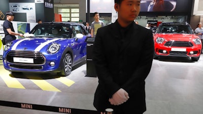 In this April 26, 2018, photo, a security guard stands near MINI cars displayed at the China Auto Show in Beijing. BMW Group and China's biggest SUV brand, Great Wall Motor, announced Tuesday, July 10, 2018, a partnership to produce electric MINI vehicles in China.