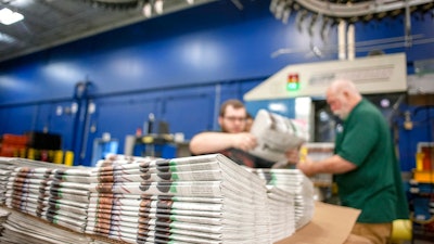 In this April 11, 2018, photo, production workers stack newspapers onto a cart at the Janesville Gazette Printing & Distribution plant in Janesville, Wis. Members of Congress are warning that newspapers in their home states are in danger of cutting coverage or going out of business if the United States maintains recently imposed tariffs on Canadian newsprint.