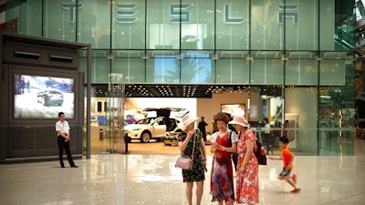 In this July 5, 2018, file photo, women look at a smartphone outside of a Tesla showroom at an upscale shopping mall in Beijing. Electric car producer Tesla will build its first factory outside the United States in Shanghai under an agreement signed Tuesday, July 10, 2018, becoming the first wholly foreign-owned automaker in China.