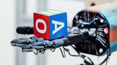 This undated photo provided by OpenAI shows a robotic hand holding a cube at the company's research lab in San Francisco. The hand, called Dactyl, has a single job, and that’s to rotate a cube until the letter facing up matches a random selection.