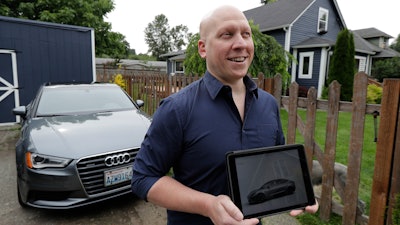 In this June 27, 2018, photo, Christian Kingery poses for photo at his home in Preston, Wash., near Seattle, next to the leased Audi he is driving until he can take delivery of a long-awaited Tesla Model 3, which is shown on his tablet computer. Kingery, who is on an official waiting list for his car, says Tesla has told him it could take until between September and November of 2018 for his car to be delivered, but he fears it might be even longer.