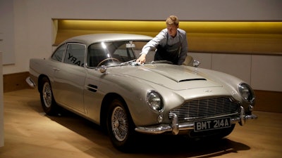 In this Tuesday, June 19, 2018 file photo, a staff member from the Bonhams motor car department poses for photographers with the 1965 Aston Martin DB5 driven by actor Pierce Brosnan in his role as James Bond in the 1995 movie GoldenEye during a photocall at premises of Bonhams auction house in London. Aston Martin, the maker of James Bond's favorite sports car, says it may sell shares for the first time as the company seeks to attract more wealthy buyers with an expanded product range including sedans, sports utility vehicles and even submarines.