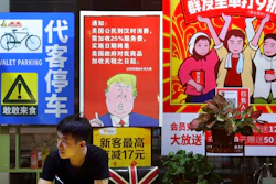 n this Monday, Aug. 13, 2018, photo, a man stands near a poster depicting a mural of U.S. President Donald Trump stating that all American customers will be charged 25 percent more than others starting from the day president Trump started the trade war against China, on display outside a restaurant in Guangzhou in south China's Guangdong province. The recent trade war between the world's two biggest economies has forced many multinational companies to reschedule purchases and rethink where they buy materials and parts to try to dodge or blunt the effects of tit-for-tat tariffs between Washington and Beijing.