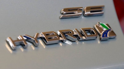 This Feb. 14, 2013, file photo shows a hybrid logo on the back of a Ford Fusion hybrid automobile at the 2013 Pittsburgh Auto Show in Pittsburgh. Ford is recalling the charging cords for more than 50,000 plug-in hybrid and electric cars in North America because they could cause fires in electrical outlets. The company says the 120-volt cords came with certain 2012 through 2015 Focus electrics and some 2013 through 2015 Fusion Energi and C-Max Energi plug-in hybrids.