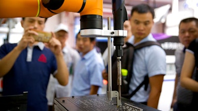 In this Aug. 15, 2018, photo, visitors look at a manufacturing robot from Chinese robot maker Aubo Robotics at the World Robot Conference in Beijing, China. The United States and China imposed more tariff hikes on billions of dollars of each other's automobiles, factory machinery and other goods Thursday, Aug. 23, 2018, in an escalation of a battle over Beijing's technology policy that companies worry will chill global economic growth.