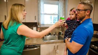 In this Aug. 1, 2018 photo, Lauren Woehr hands her 16-month-old daughter Caroline, held by her husband Dan McDowell, a cup filled with bottled water at their home in Horsham, Pa. In Horsham and surrounding towns in eastern Pennsylvania, and at other sites around the United States, the foams once used routinely in firefighting training at military bases contained per-and polyfluoroalkyl substances, or PFAS. EPA testing between 2013 and 2015 found significant amounts of PFAS in public water supplies in 33 U.S. states.