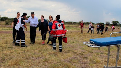 In this photo released by Red Cross Durango communications office, Red Cross workers attend airline passengers who survived a plane crash, as they walk away from the crash site in a field near the airport in Durango, Mexico, Tuesday, July 31, 2018. An Aeromexico jetliner crashed while taking off during a severe storm, smacking down in a field nearly intact then catching fire, and officials said it appeared everyone on board escaped the flames.