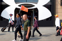 A Chinese tour guide leads a tour group past a store from American sportswear retailer Under Armour at an outdoor shopping area in Beijing, Tuesday, Sept. 25, 2018. A Chinese trade envoy said Tuesday that talks with Washington are impossible while the United States 'holds a knife' to Beijing's neck by imposing tariff hikes.
