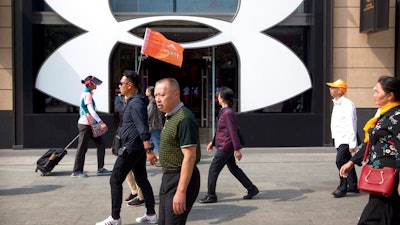 A Chinese tour guide leads a tour group past a store from American sportswear retailer Under Armour at an outdoor shopping area in Beijing, Tuesday, Sept. 25, 2018. A Chinese trade envoy said Tuesday that talks with Washington are impossible while the United States 'holds a knife' to Beijing's neck by imposing tariff hikes.