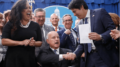 State Sen. Kevin de Leon, D-Los Angeles, second from right, displays his environmental measure SB100 after is was signed into law by Calif., Gov. Jerry Brown front center, Monday, Sept. 10, 2018, in Sacramento, Calif. Brown, surrounded by lawmakers and activists including Assembly members Lorena Gonzalez Fletcher, of San Diego, second from left, Ken Cooley, of Rancho Cordova, third from left and billionaire activist Tom Steyer, right, signed SB100 which sets a goal of phasing out all fossil fuels from the state's electricity sector by 2045.