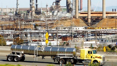 This March 9, 2010, file photo shows a tanker truck passing the Chevron oil refinery in Richmond, Calif. Federal officials say Chevron Corp. has agreed to pay a nearly $3 million fine and spend $160 million on environmental improvements and upgrading oil refineries to resolve allegations the company violated pollution laws. The U.S. Department of Justice announced the agreement Wednesday, Oct. 24, 2018.