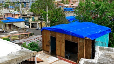 In this Oct. 19, 2017, file photo, homes in the Cantera area are covered with FEMA tarps, where buildings from the Hato Rey area stand in the background in San Juan, Puerto Rico. A new law requires the Federal Emergency Management Agency to investigate how it came to award Hurricane Maria relief contracts to a company with an unproven record. The Associated Press reported last year that the newly-formed contractor, Florida-based Bronze Star, LLC, won more than $30 million in FEMA contracts but never delivered the emergency tarps and plastic sheeting for repairs of damaged homes in Puerto Rico.