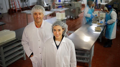 In this Tuesday, Oct. 2, 2018, photo Ollie co-founders Gabby Slome and Alex Douzet pose for a picture at the manufacturing facility where their dog food is made in Woodbridge, N.J. Potential customers or investors often assume that Slome and Douzet, two of the co-founders of dog food manufacturer Ollie, are married. Outsiders can't seem to get their minds around the fact that Slome, who's married to someone else, could be running a business without her husband, or without him bankrolling her.