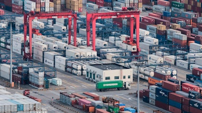 In this March 29, 2018, file photo, a cargo truck drives amid stacked shipping containers at the Yangshan port in Shanghai.