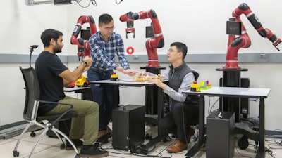 Using a handheld device, Ajay Mandelkar, Jim Fan and Yuke Zhu use their software to control a robot arm.