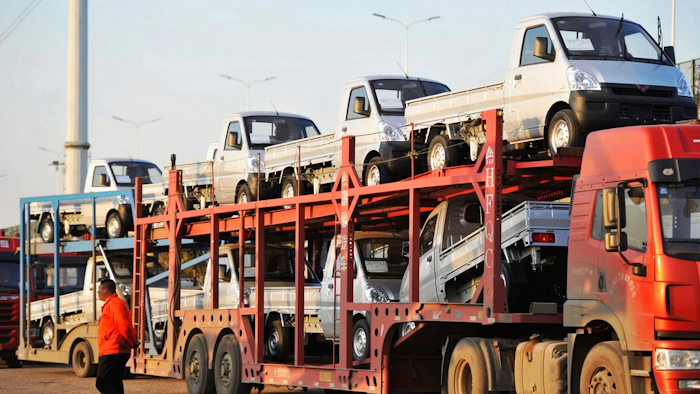 In this Oct. 31, 2018, photo, a staff members walks past a semi truck loaded with new vehicles in the parking lot for a local automaker in Qingdao in eastern China's Shandong province. China's auto sales sank for a fourth month in October, tumbling 13 percent from a year earlier and adding to an unexpectedly painful downturn for global automakers in their biggest market.