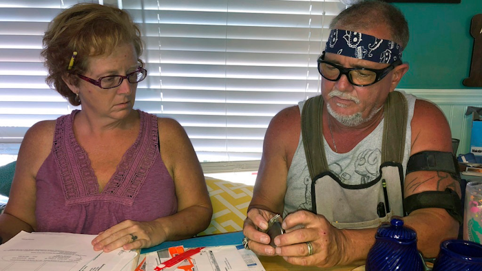 In this Oct. 31 2018 photo, George and Brenda Davis look at his nerve stimulator and medical documents at their home in Milton, Fla. George Davis had three Medtronic spinal-cord implants between 2003 and 2007 after a car accident mangled his back. They temporarily reduced some of his pain, but he said the non-rechargeable batteries that were supposed to last for years never did and he tired of multiple surgical removals. In 2015, he decided to try a Boston Scientific device. But he said he soon started feeling pain shooting down his back and legs and a burning sensation at the implant site. Brenda Davis said Boston Scientific disregarded her complaints after her husband suffered a life-threatening infection following implant surgery.