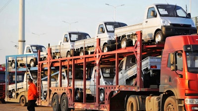 In this Oct. 31, 2018, photo, a staff members walks past a semi truck loaded with new vehicles in the parking lot for a local automaker in Qingdao in eastern China's Shandong province. China's auto sales sank for a fourth month in October, tumbling 13 percent from a year earlier and adding to an unexpectedly painful downturn for global automakers in their biggest market.