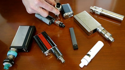 In this Tuesday, April 10, 2018, file photo, a high school principal displays vaping devices that were confiscated from students in such places as restrooms or hallways at the school in Massachusetts. The Food and Drug Administration is planning on requiring strict limits on the sale of most flavored e-cigarettes, including age verification controls for online sales, in an effort to curtail their use among children and teenagers. FDA officials tell The Wall Street Journal on Thursday, Nov. 8, the actions are expected to be announced as early as the following week.