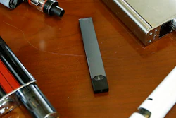 This Tuesday, April 10, 2018 file photo shows vaping devices, including a Juul, center, that were confiscated from students at a high school in Marshfield, Mass. On Tuesday, Nov. 13, 2018, San Francisco-based Juul Labs Inc. announced it had stopped filling orders for its mango, fruit, creme and cucumber pods but not menthol and mint. It will sell all flavors through its website and limit sales to those 21 and older.