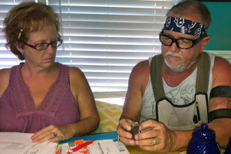 In this Oct. 31 2018 photo, George and Brenda Davis look at his nerve stimulator and medical documents at their home in Milton, Fla. George Davis had three Medtronic spinal-cord implants between 2003 and 2007 after a car accident mangled his back. They temporarily reduced some of his pain, but he said the non-rechargeable batteries that were supposed to last for years never did and he tired of multiple surgical removals. In 2015, he decided to try a Boston Scientific device. But he said he soon started feeling pain shooting down his back and legs and a burning sensation at the implant site. Brenda Davis said Boston Scientific disregarded her complaints after her husband suffered a life-threatening infection following implant surgery.