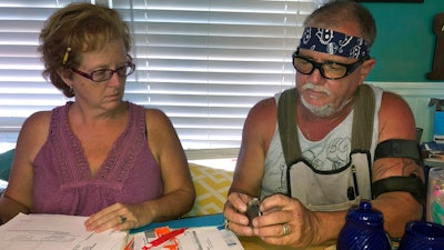 In this Oct. 31 2018 photo, George and Brenda Davis look at his nerve stimulator and medical documents at their home in Milton, Fla. George Davis had three Medtronic spinal-cord implants between 2003 and 2007 after a car accident mangled his back. They temporarily reduced some of his pain, but he said the non-rechargeable batteries that were supposed to last for years never did and he tired of multiple surgical removals. In 2015, he decided to try a Boston Scientific device. But he said he soon started feeling pain shooting down his back and legs and a burning sensation at the implant site. Brenda Davis said Boston Scientific disregarded her complaints after her husband suffered a life-threatening infection following implant surgery.