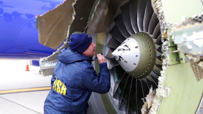 In this April 17, 2018, file photo, a National Transportation Safety Board investigator examines damage to the engine of the Southwest Airlines plane that made an emergency landing at Philadelphia International Airport in Philadelphia. In new accounts released Wednesday, Nov. 14, into the April accident, the flight attendants described being unable to bring the woman back in the plane until two male passengers stepped in to help. The flight attendants told investigators at least one of the men put his arm out of the window and wrapped it around the woman’s shoulder to help pull her back in.