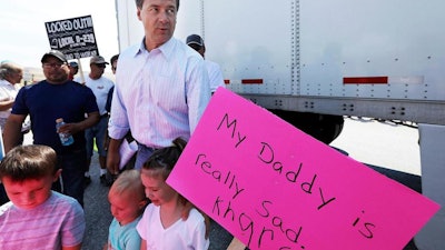 In this Aug. 9, 2018, file photo, Montana Gov. Steve Bullock stands with children holding picket signs as a semitruck leaves Imerys America's talc-milling plant in Three Forks, Mont. Locked-out union workers have approved a three-year contract with the owners of a talc-milling plant in Montana after 90 days on the picket lines.