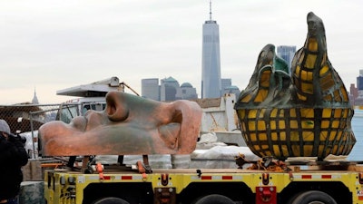 The original torch of the Statue of Liberty, and a replica of her face, rest on a hydraulically stabilized transporter, Thursday, Nov. 15, 2018 in New York. The torch, which was removed in 1984 and replaced by a replica, was being moved into what will become its permanent home at a new museum on Liberty Island. New York's One World Trade Center is visible, background center.