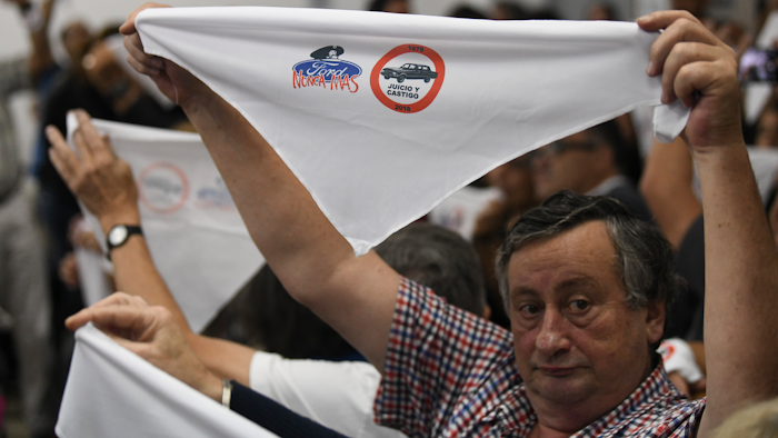 Family members of ex-Ford Motor Co. employees hold up handkerchiefs that are stamped with a message that reads in Spanish: “Ford never more” in a courtroom.