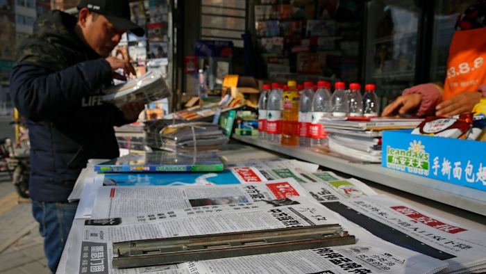 A man arranges magazines near newspapers with the headlines of China outcry against U.S. on the detention of Huawei's chief financial officer, Meng Wanzhou, at a news stand in Beijing, Monday, Dec. 10, 2018. China has summoned the U.S. ambassador to Beijing to protest Canada's detention of an executive of Chinese electronics giant Huawei at Washington's behest and demand the U.S. cancel an order for her arrest.