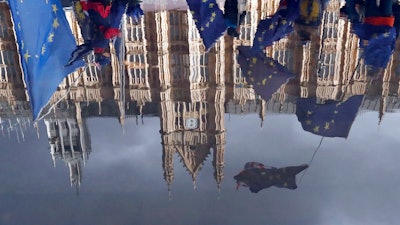 Protestors are reflected in a puddle as they wave European flags to demonstrate against Brexit in front of the Parliament in London, Monday, Dec. 3, 2018.