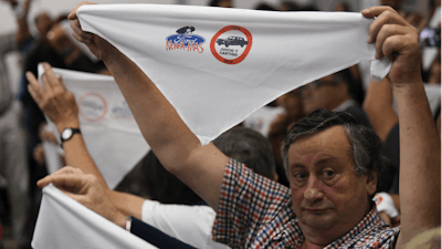 Family members of ex-Ford Motor Co. employees hold up handkerchiefs that are stamped with a message that reads in Spanish: “Ford never more” in a courtroom.