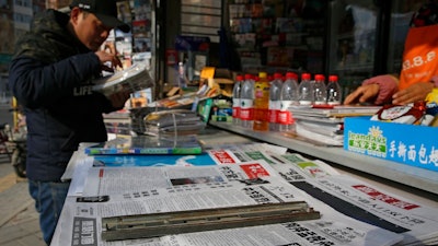 A man arranges magazines near newspapers with the headlines of China outcry against U.S. on the detention of Huawei's chief financial officer, Meng Wanzhou, at a news stand in Beijing, Monday, Dec. 10, 2018. China has summoned the U.S. ambassador to Beijing to protest Canada's detention of an executive of Chinese electronics giant Huawei at Washington's behest and demand the U.S. cancel an order for her arrest.