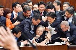 Japan's opposition parties' members try to stop Judicial Affairs Committee Chairman Shinichi Yokoyama, bottom center, from moving to hold a vote for a bill to revise an immigration control law, at upper house committee in Tokyo early Saturday, Dec. 8, 2018. Japan is preparing to officially open the door to foreign workers to do unskilled jobs and possibly eventually become citizens.