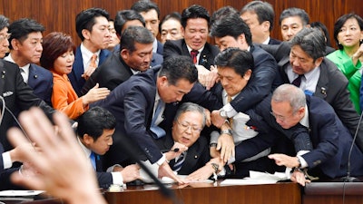 Japan's opposition parties' members try to stop Judicial Affairs Committee Chairman Shinichi Yokoyama, bottom center, from moving to hold a vote for a bill to revise an immigration control law, at upper house committee in Tokyo early Saturday, Dec. 8, 2018. Japan is preparing to officially open the door to foreign workers to do unskilled jobs and possibly eventually become citizens.