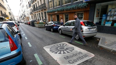 A man looks at a sign painted on the road indicating the boundary of the centre of the city as he crosses the street in Madrid, Spain, Friday, Nov. 30, 2018. Madrid activated a new traffic restriction system Friday in an attempt to reduce pollution in the city. Petrol vehicles before 2000 and diesel ones registered before 2006 are banned from this central area but on the first day of the restrictions, drivers will not be fined as municipal police were only warning drivers of the new restrictions.