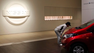 A man inspects car in front of the logo of the Nissan Motor Co. at its global headquarters in Yokohama, near Tokyo, Monday, Dec. 17, 2018. Nissan's board met Monday but failed to pick a new chairman to replace Carlos Ghosn, arrested last month on charges of violating financial regulations, saying more discussion was needed.