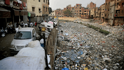 In this Saturday, Dec. 8, 2018 photo piles of electronic waste is placed next to a drain chocked with plastic and garbage in New Delhi, India.