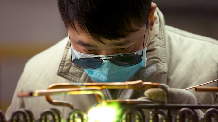 In this Friday, Feb. 24, 2017, file photo, a factory worker uses a gas torch on an air conditioning condenser unit in a factory in Jiaozhou, eastern China's Shandong Province. An official survey shows China’s manufacturing activity contracted in December, boosting pressure on Beijing to reverse an economic downturn amid trade tension with Washington.