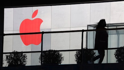 In this Dec. 6, 2018, photo, a woman runs past a Apple logo colored red in Beijing, China. Apple Inc.’s $1,000 iPhone is a tough sell to Chinese consumers who are jittery over an economic slump and a trade war with Washington. The tech giant became the latest global company to collide with Chinese consumer anxiety when CEO Tim Cook said iPhone demand is waning, due mostly to China. Weak consumer demand in the world’s second-largest economy is a blow to industries from autos to designer clothing that are counting on China to drive revenue growth.