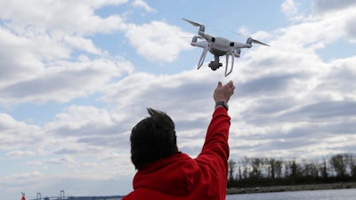 In this April 29, 2018, file photo, a drone operator helps to retrieve a drone after photographing over Hart Island in New York. Federal officials plan to ease restrictions on flying drones over crowds and at night. Federal officials plan to ease restrictions on flying small drones over crowds and at night, which would give a boost to the commercial use of unmanned aircraft. The Federal Aviation Administration outlined draft rules Monday, Jan. 14, 2019, that would let drone operators do those things without a special waiver from current rules.