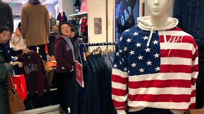 A woman tries out a sweater at a U.S. retailer GAP's flagship store in Beijing, Thursday, Jan. 10, 2019. Uncertainty over the outcome of China-U.S. trade talks is casting a pall over Asian markets as both sides kept quiet about what lies ahead.