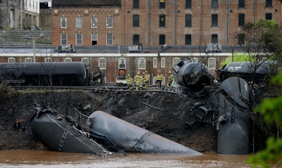 In this April 30, 2014 file photo, firefighters and rescue workers work along the tracks where several CSX tanker cars carrying crude oil derailed and caught fire along the James River near downtown in Lynchburg, Virginia.