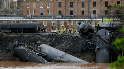 In this April 30, 2014 file photo, firefighters and rescue workers work along the tracks where several CSX tanker cars carrying crude oil derailed and caught fire along the James River near downtown in Lynchburg, Virginia.