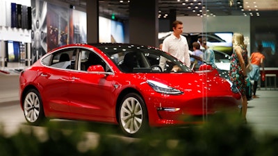 In this July 6, 2018, file photo, a prospective customer confer with sales associate as a Model 3 sits on display in a Tesla showroom in the Cherry Creek Mall in Denver. On Tuesday, Jan. 1, 2019, the federal credit for Tesla buyers dropped from $7,500 to $3,750. It will gradually be phased out this year.